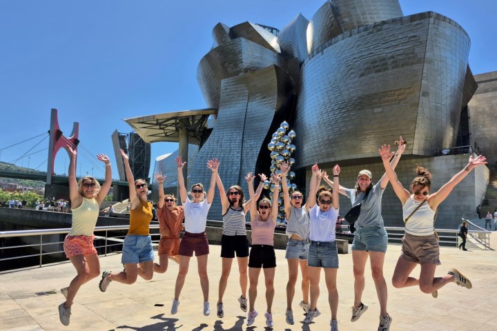 Group of people jumping joyfully in front of a modern art museum.