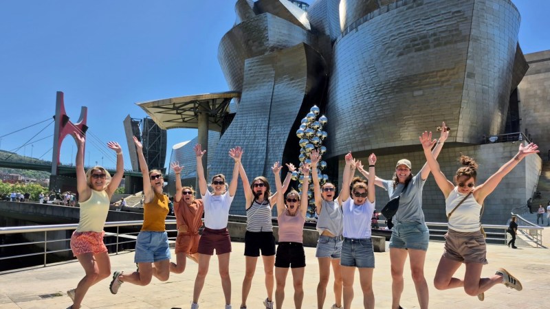 Group of people jumping in front of a modern metallic building under a clear blue sky.