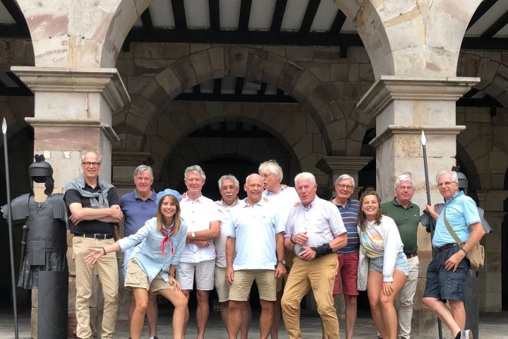 Group of people posing in front of a stone archway with spears displayed nearby.
