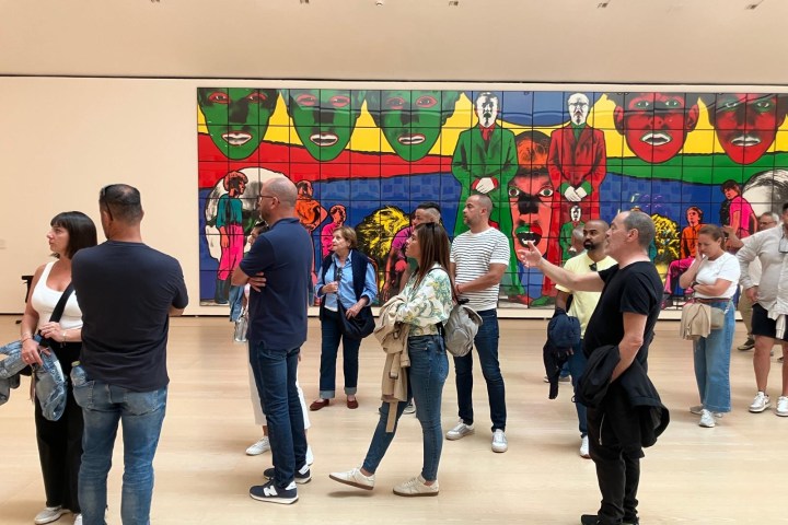 People standing in an art gallery, observing a large colorful mural on the wall.