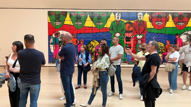 People standing in an art gallery, observing a large colorful mural on the wall.