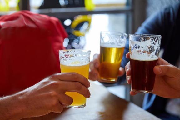Hands clinking three glasses of beer in a toast.