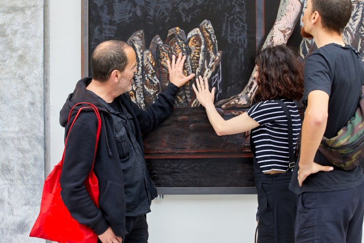 Three people engaging with tactile artwork, touching a textured painting on the wall.