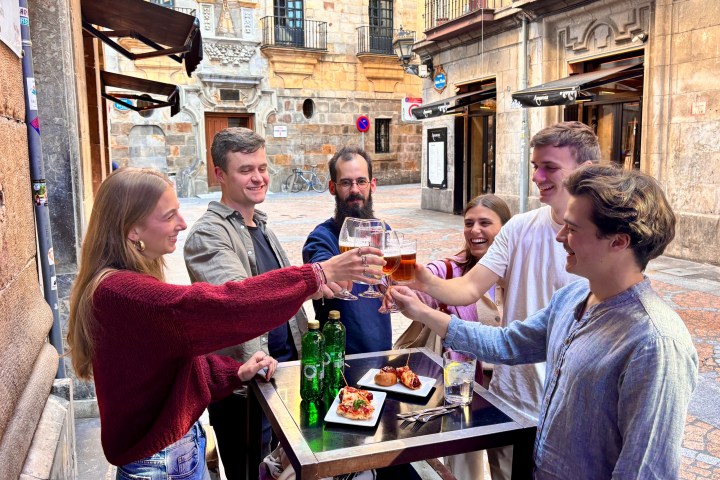 Group of adults toasting drinks at an outdoor table in a historic European street.