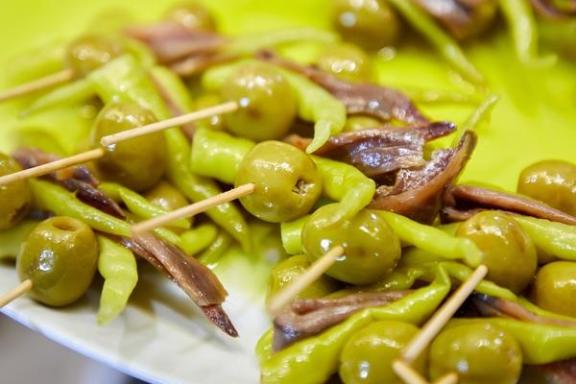Skewers with olives, anchovies, and green peppers on a plate.