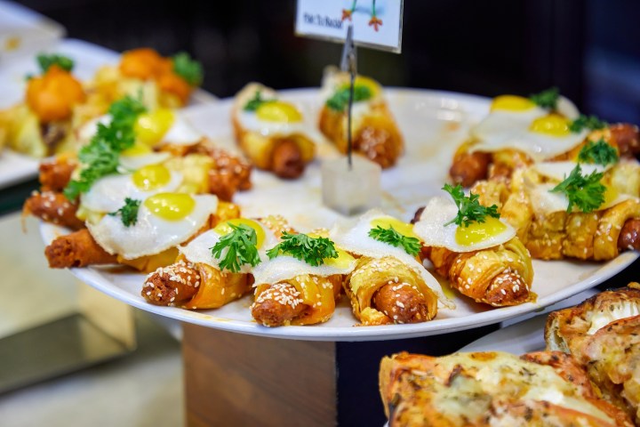 Plate of sausage croissants with fried eggs and parsley garnish.