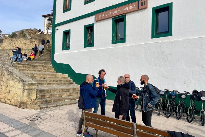 Group of men with drinks outside Portu Zaharra Taberna near stone steps.