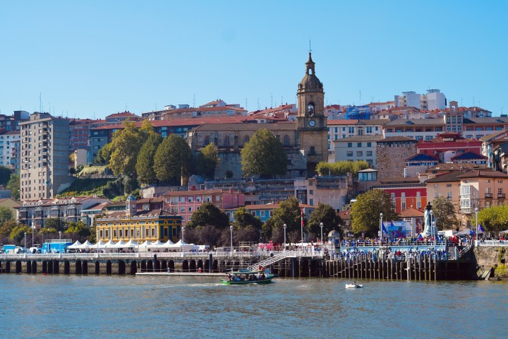 Riverside town with clock tower, colorful buildings, and boats on a sunny day.