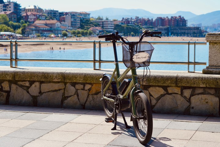 Bicycle parked on promenade with beach, water, and cityscape in background.