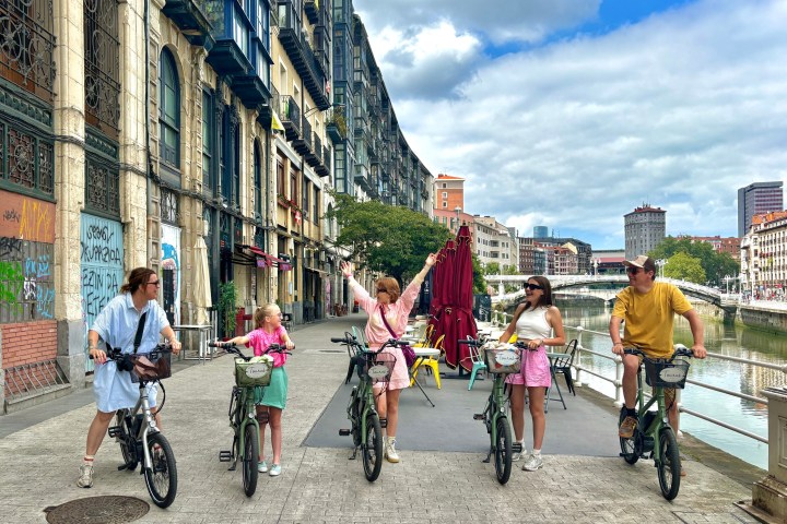 Group of five people on bicycles by a city canal with historic buildings.