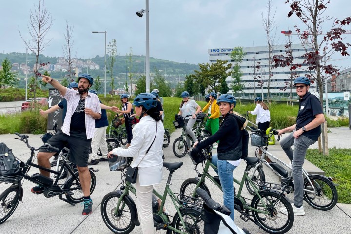 Group of cyclists with helmets gathered in an outdoor urban area.
