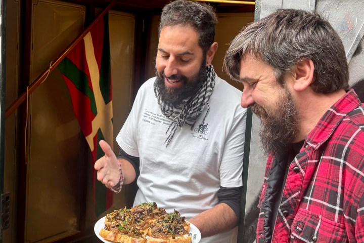 Two men smiling at a plate of food with a flag in the background.