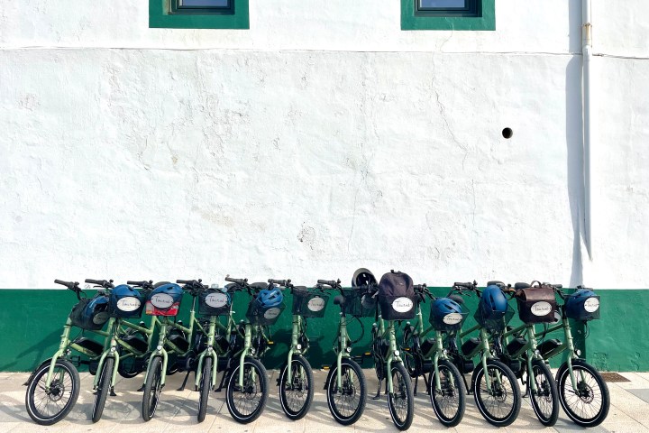 Row of green bicycles with helmets against a white and green wall.