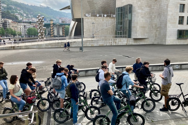 Group of people on bicycles gathered outside a large modern building.