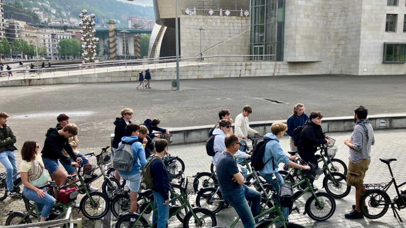Group of people on bicycles gathered outside a large modern building.