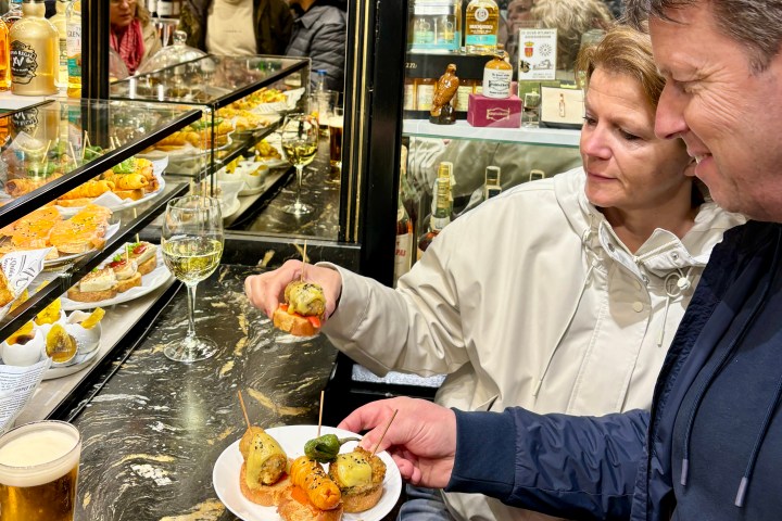 Two people enjoying tapas in a bar with various dishes and drinks displayed.