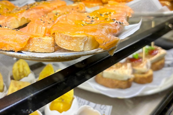 Assorted tapas with smoked salmon, mini skewers, and desserts in a display case.