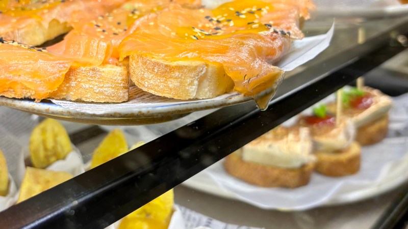 Assorted tapas with smoked salmon, mini skewers, and desserts in a display case.