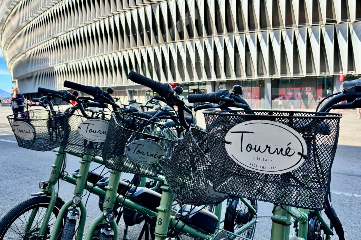 Row of rental bikes with 'Tourné' signs near a modern building.