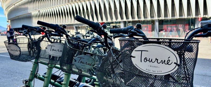 Row of rental bikes with 'Tourné' signs near a modern building.