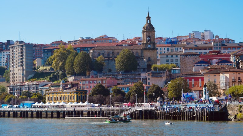 Scenic view of a riverside city with colorful buildings and a prominent clock tower.