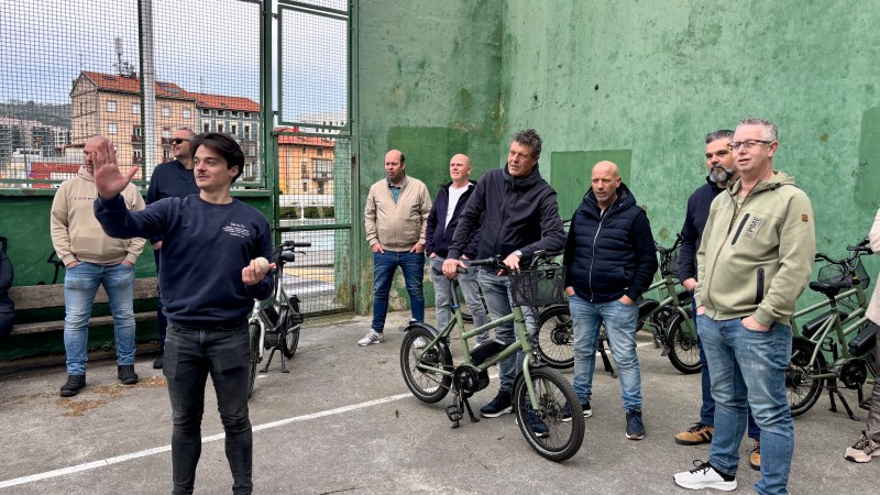 A group of people stand with bicycles in an outdoor area with green walls.