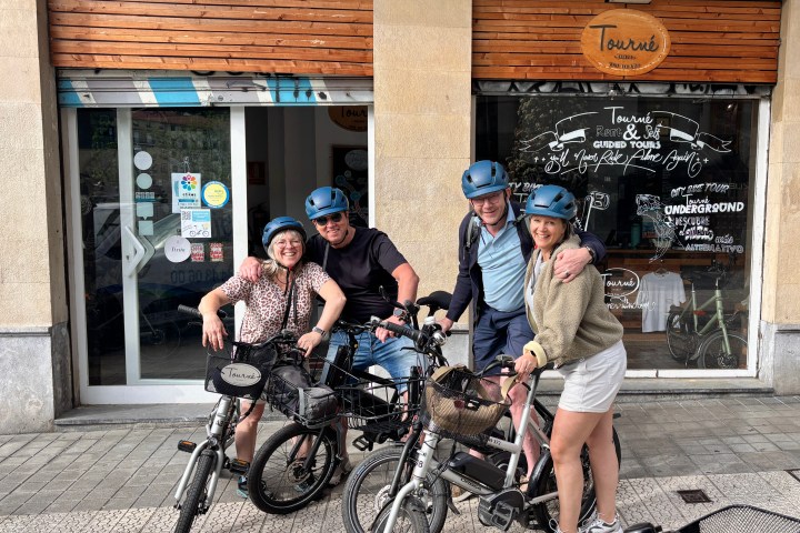 Four people with helmets posing with bikes outside a rental shop.