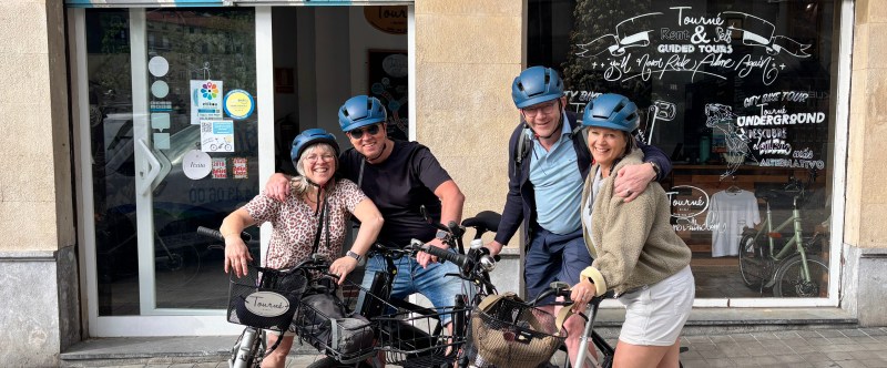 Four people with helmets posing with bikes outside a rental shop.