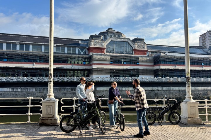 People with bicycles on a promenade near a large building.