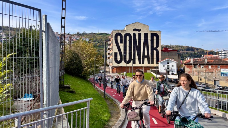 Cyclists on a red bike path beside a building with large 'SOÑAR' text.