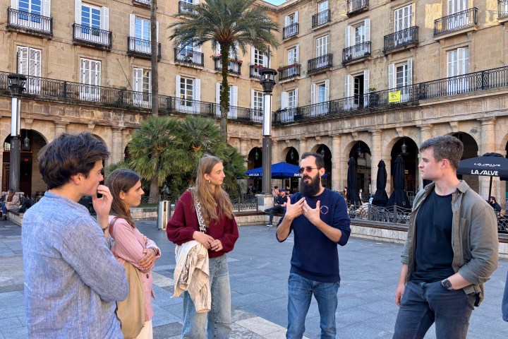 Group of people talking in a sunny plaza with historic buildings.
