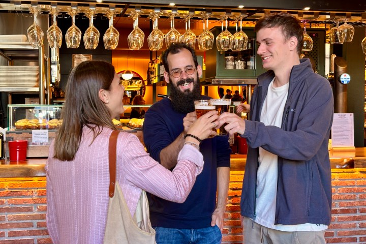 Three people smiling and toasting with beer glasses in a bar.