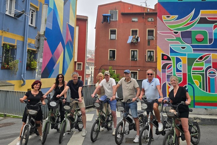 Group of people on bicycles in front of colorful murals on urban street.