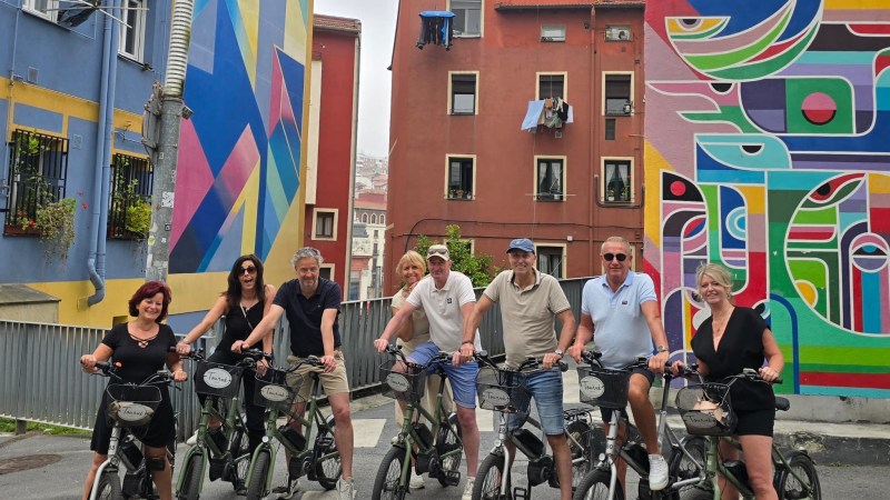 Group of people on bicycles in front of colorful murals on urban street.