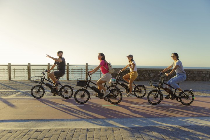 Four people riding bikes along a seaside path at sunset.