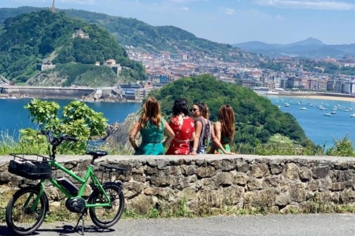 Four people and a bicycle overlooking a coastal city with hills and ocean.