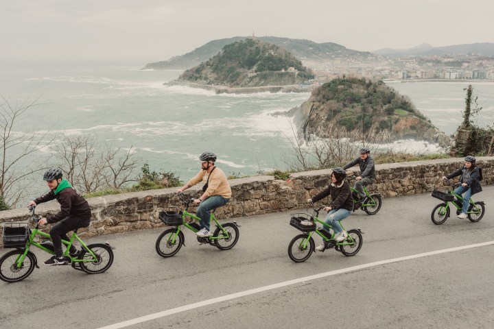 Five people ride green electric bikes along a coastal road with scenic ocean views.
