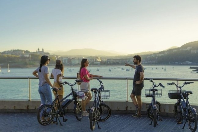 Four people with bikes overlook a scenic waterfront beneath a clear sky at sunset.