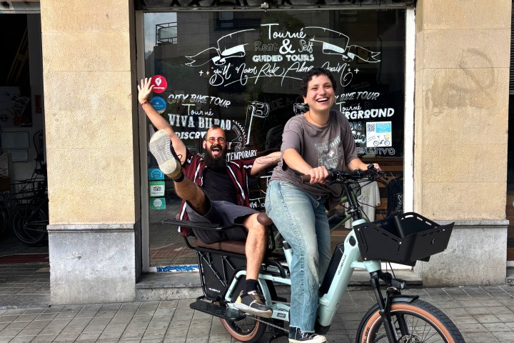 Two people smiling on a cargo bike outside a bike rental and tour shop in Bilbao