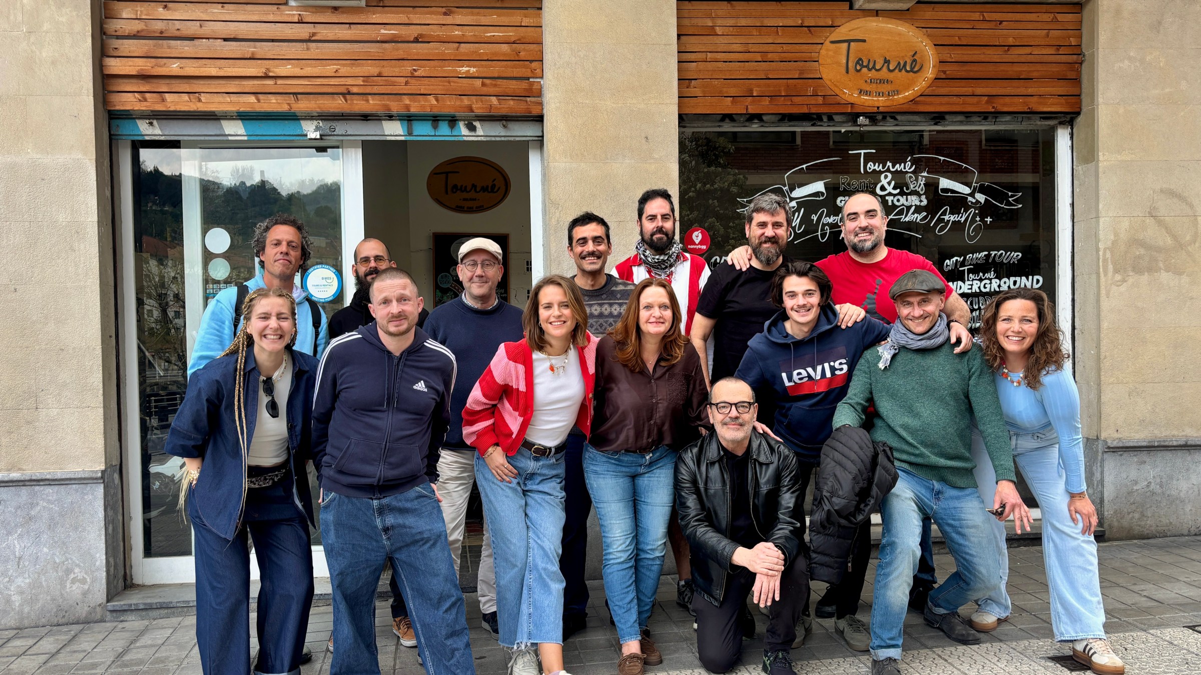 Group of people smiling in front of a storefront with a 'Tourné' sign.